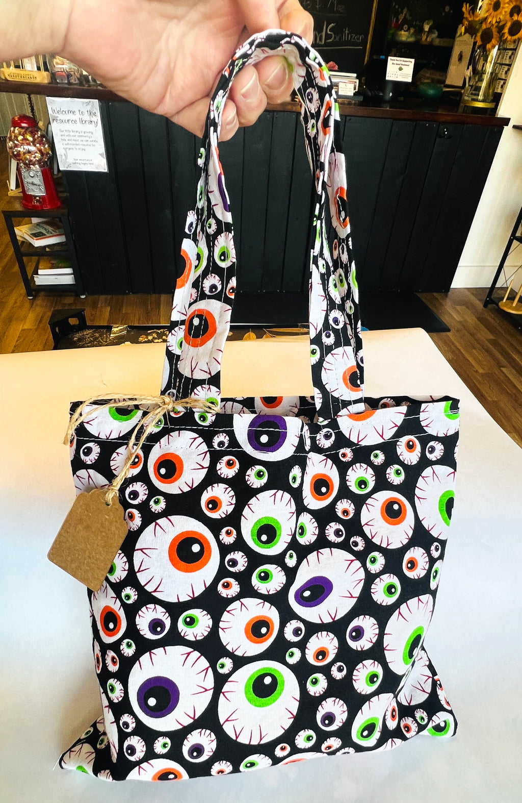 Eyeball fabric  tote bag , held up by a hand with white and shop area background 