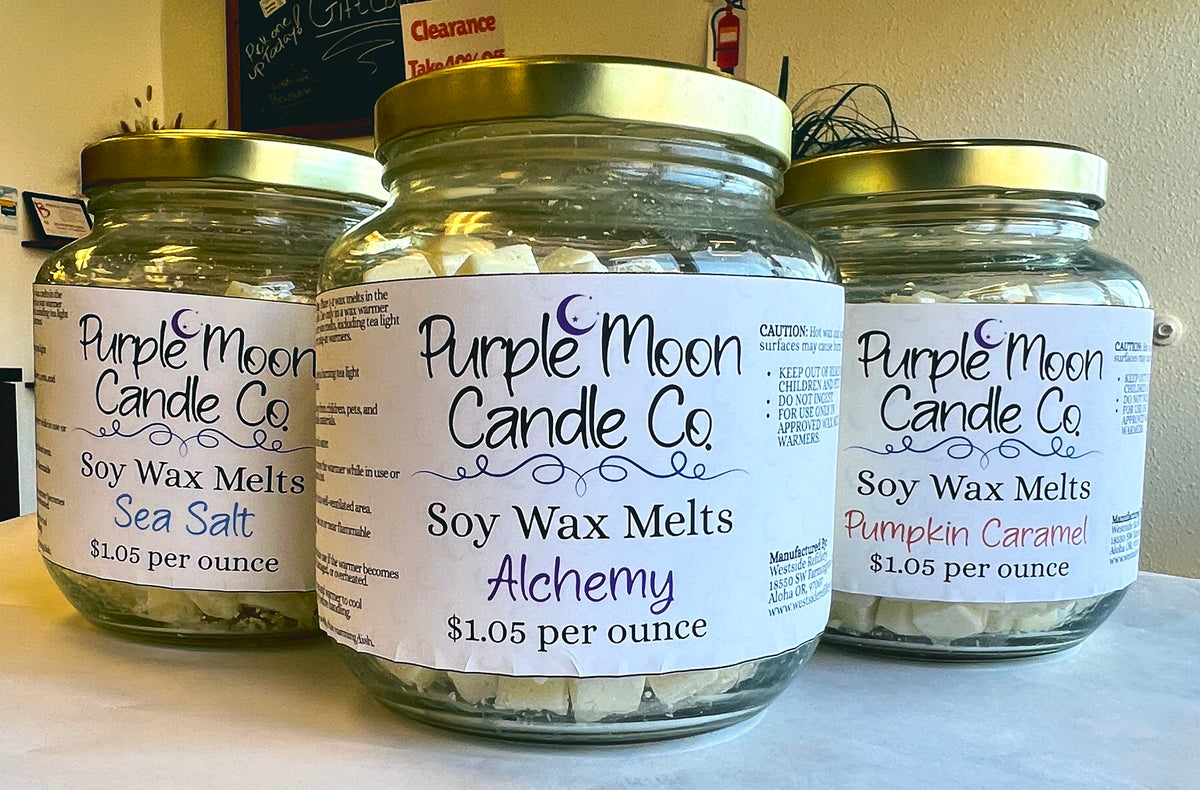 Three glass jars of Purple Moon Candle Co. soy wax melts with gold lids on a tabletop, featuring Sea Salt, Alchemy, and Pumpkin Caramel scents.
