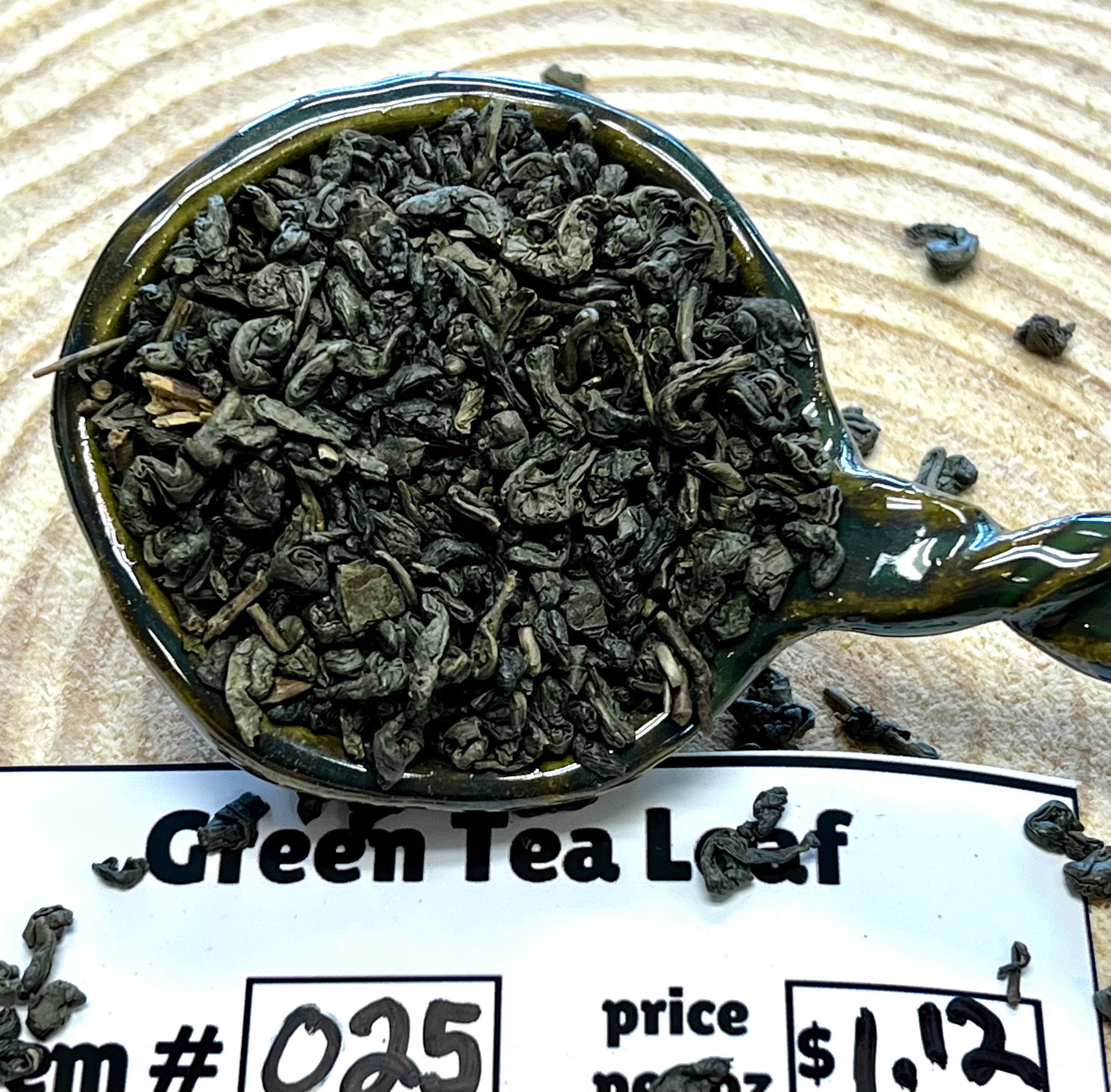 Spoon filled with green tea leaves on a wooden surface with a label below.
