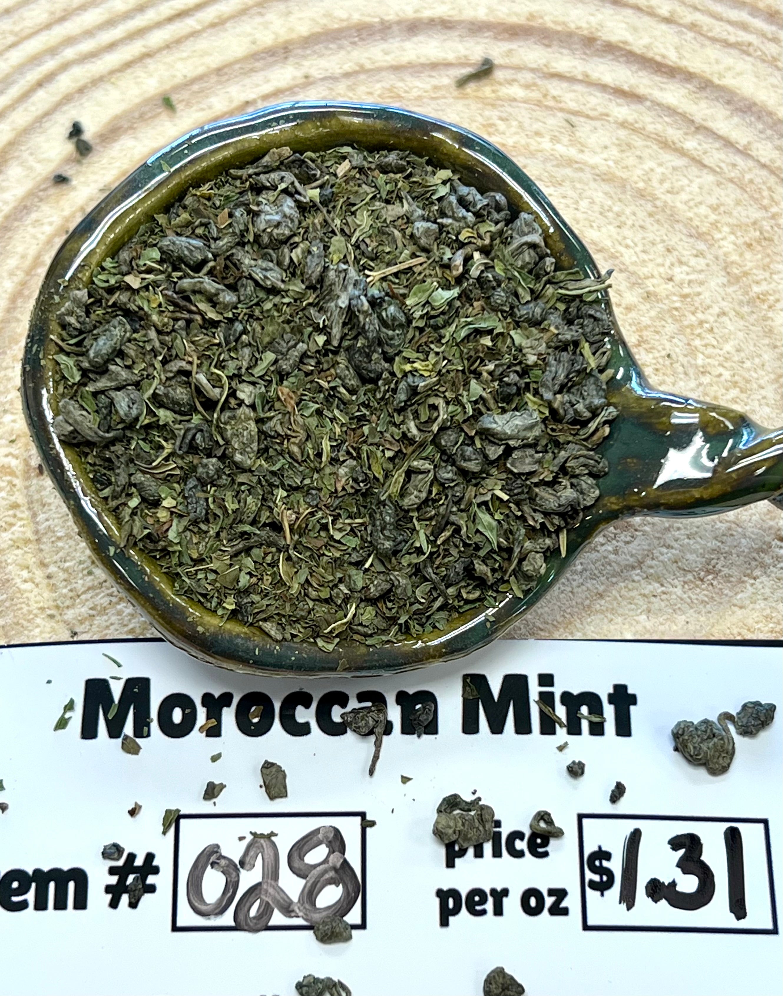 Moroccan mint in a teabag with price and item number information on a wooden surface.