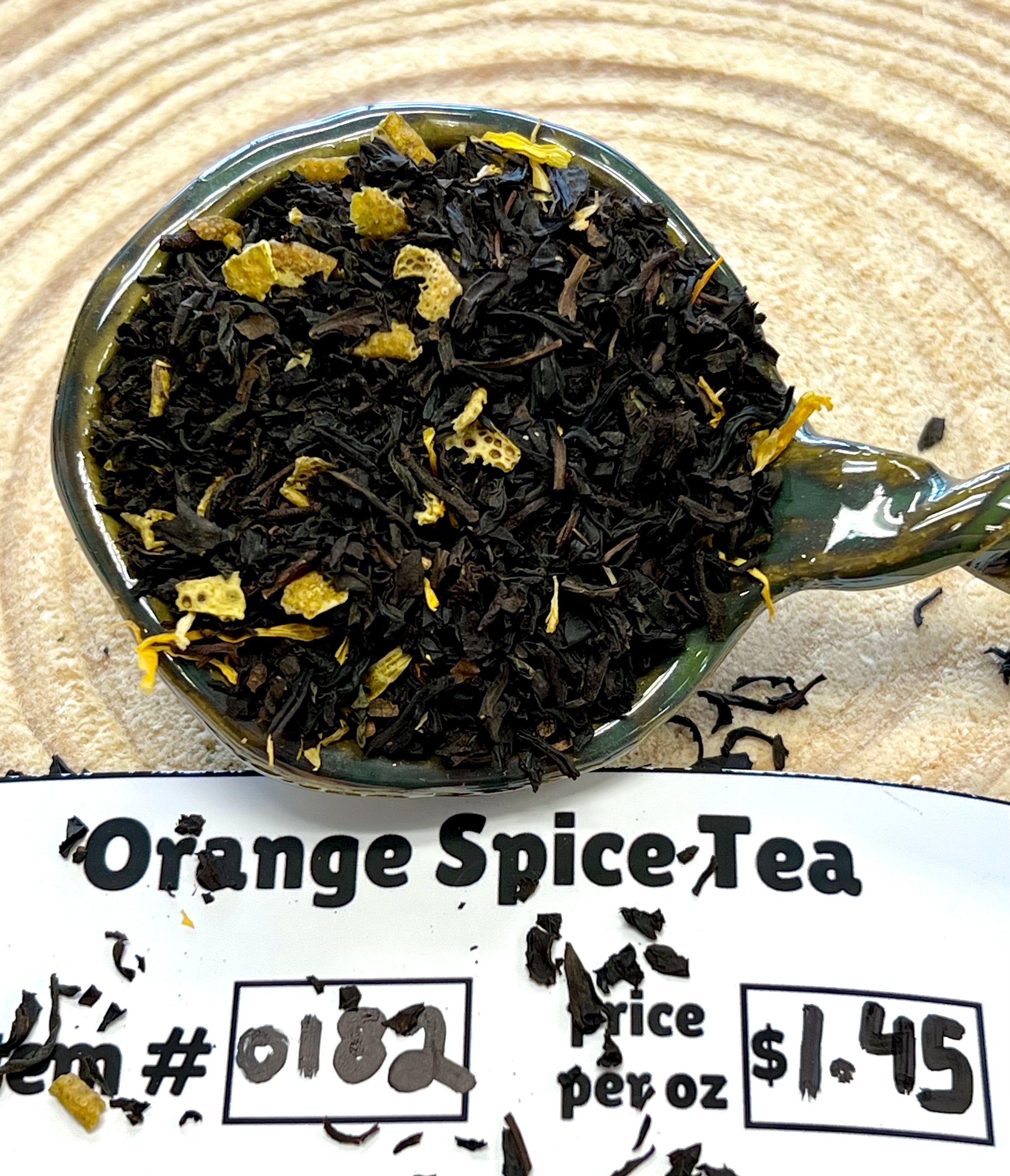 Spoon filled with black tea leaves labeled 'Orange Spice Tea' on a textured surface.