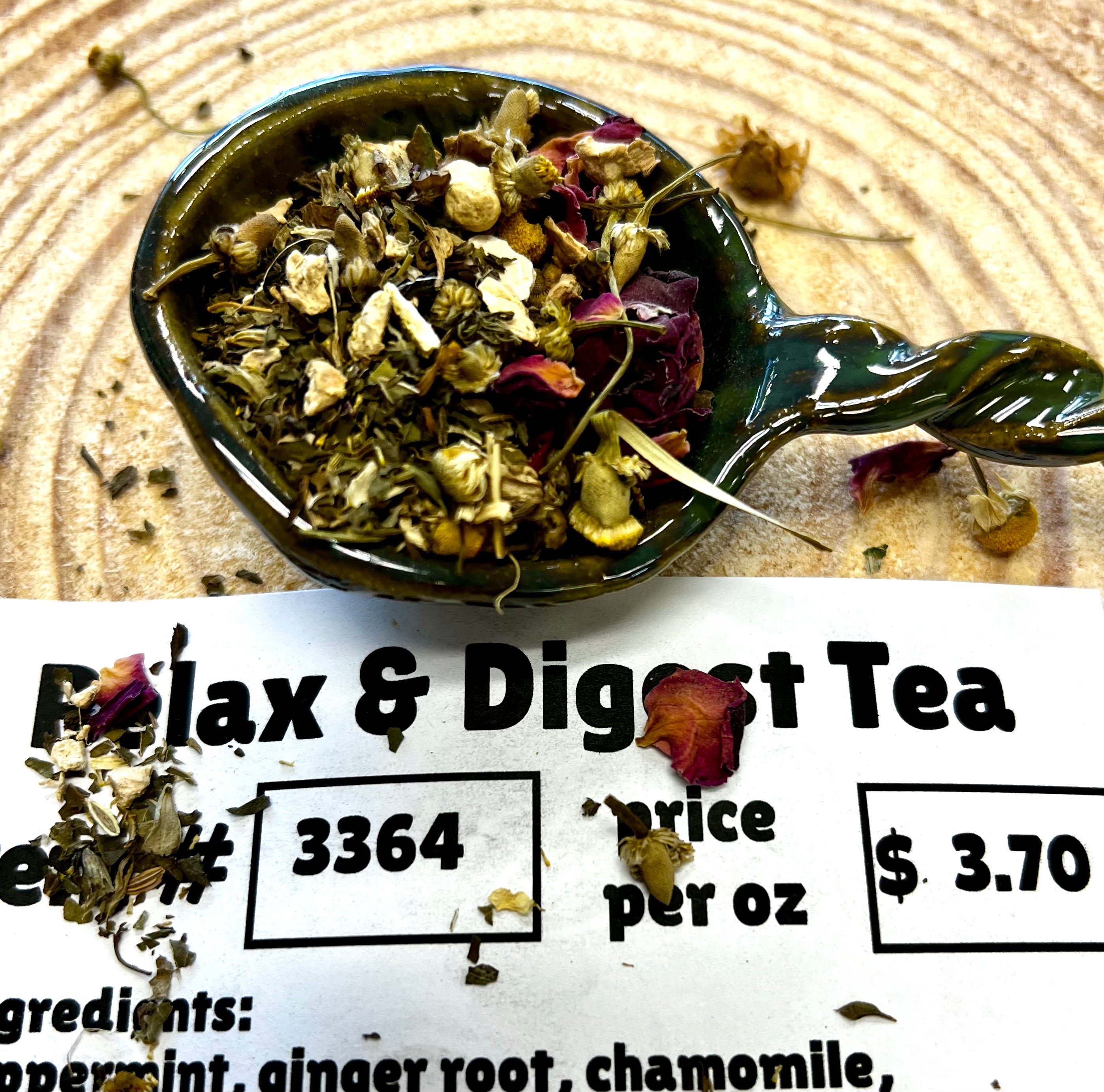 Tea leaves and flower petals in a spoon with a label below on a wooden surface
