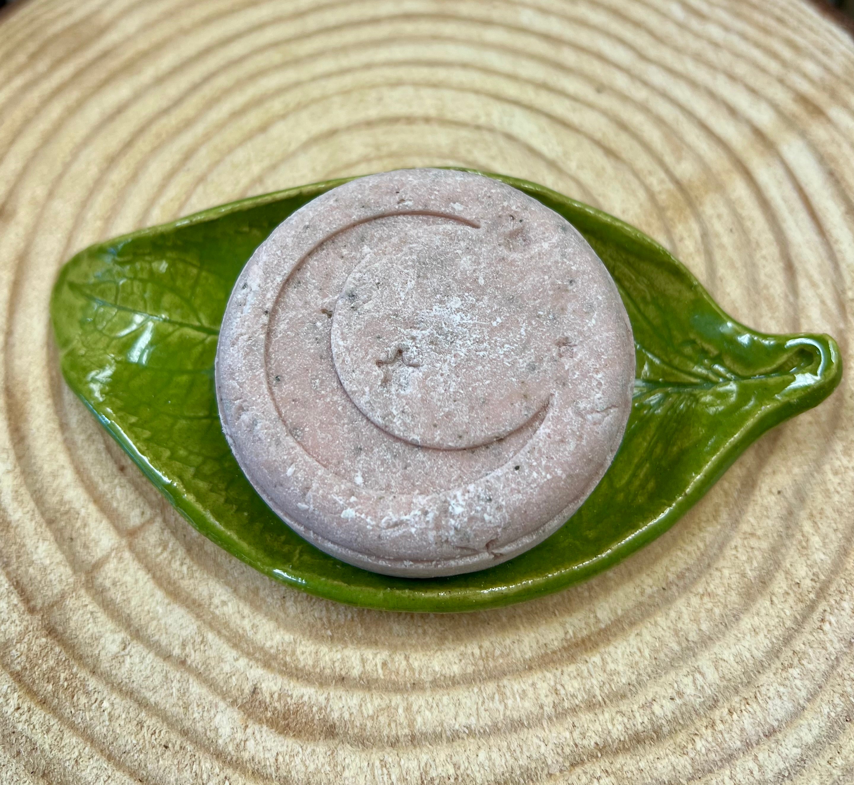 Pink Shampoo bar with star & crescent moon design on a green leaf-shaped dish on a wood surface.