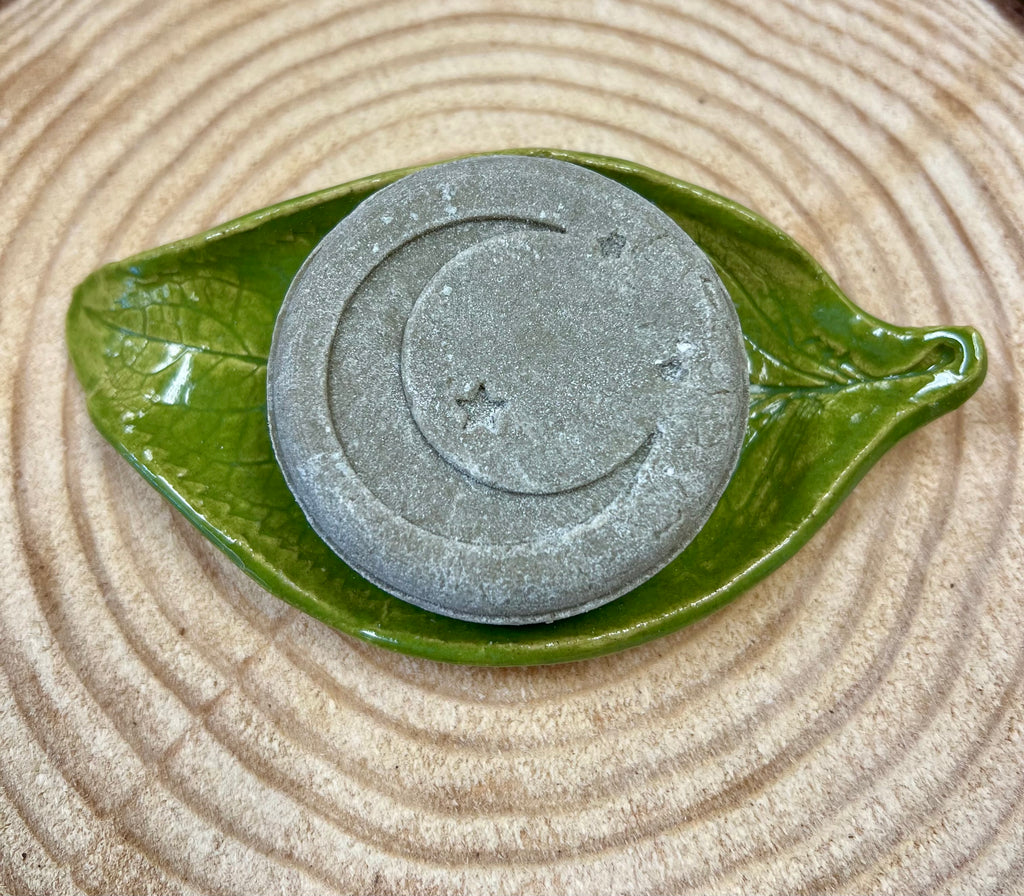 Stone color Shampoo bar with star & crescent moon design on a green leaf-shaped dish on a wood surface.