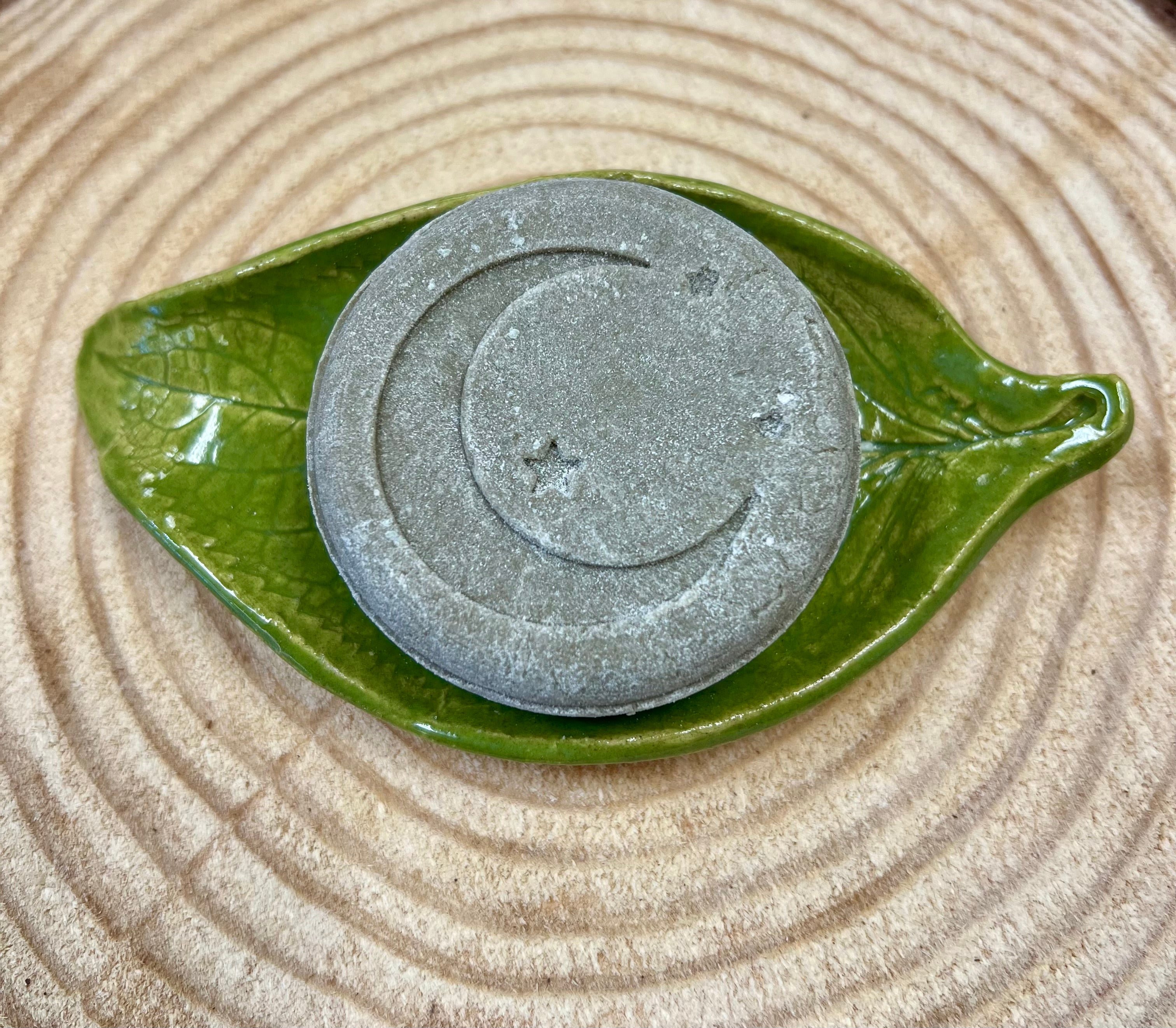 Stone color Shampoo bar with star & crescent moon design on a green leaf-shaped dish on a wood surface.