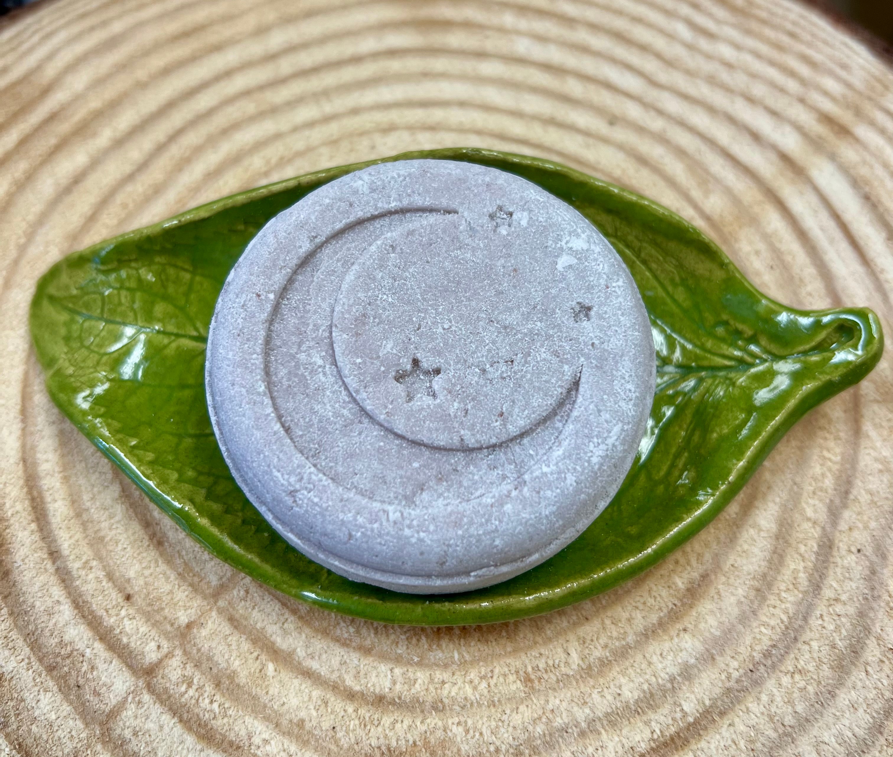 Shampoo bar with star & crescent moon design on a green leaf-shaped dish on a wood surface.