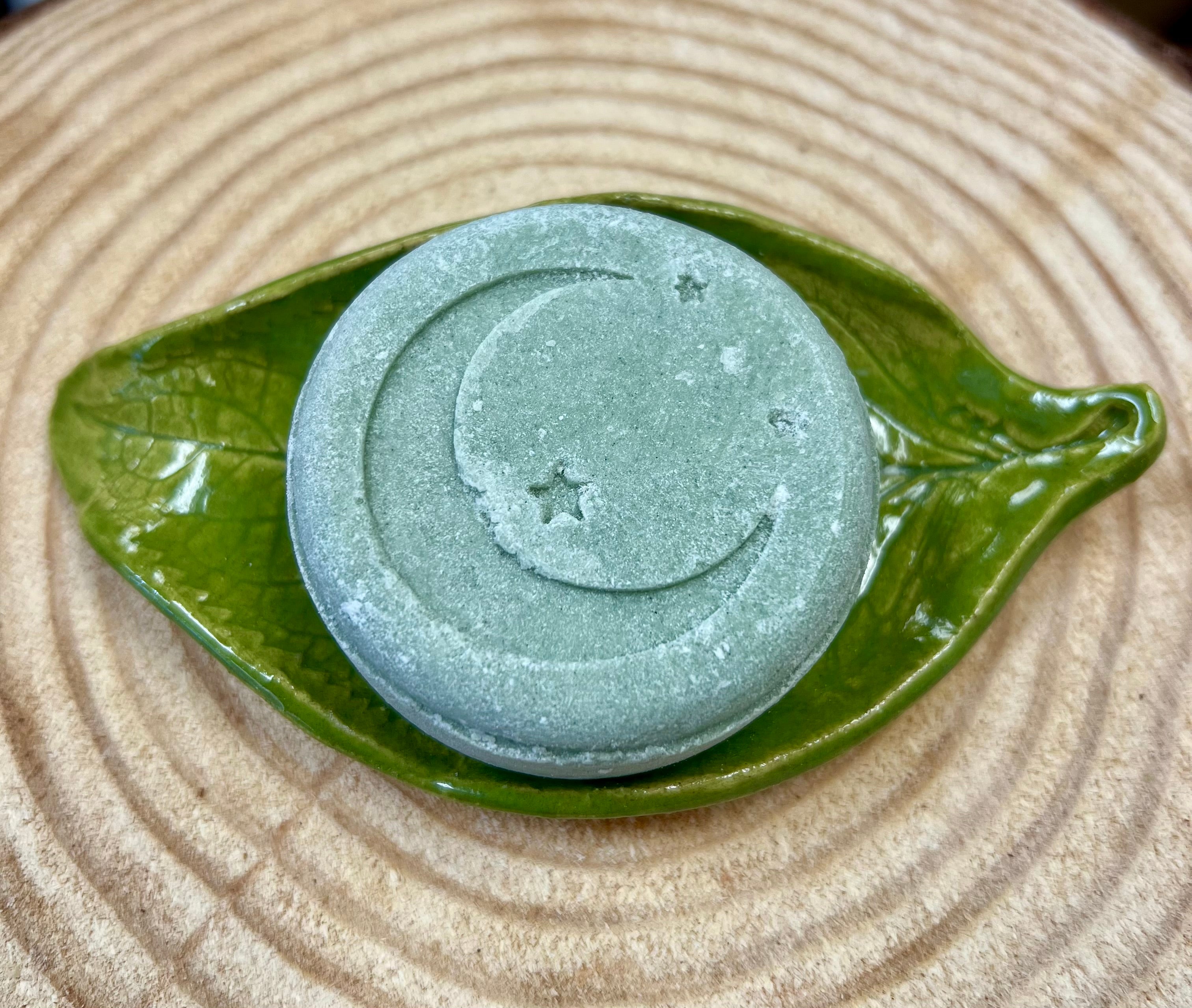Green Shampoo bar with star & crescent moon design on a green leaf-shaped dish on a wood surface.