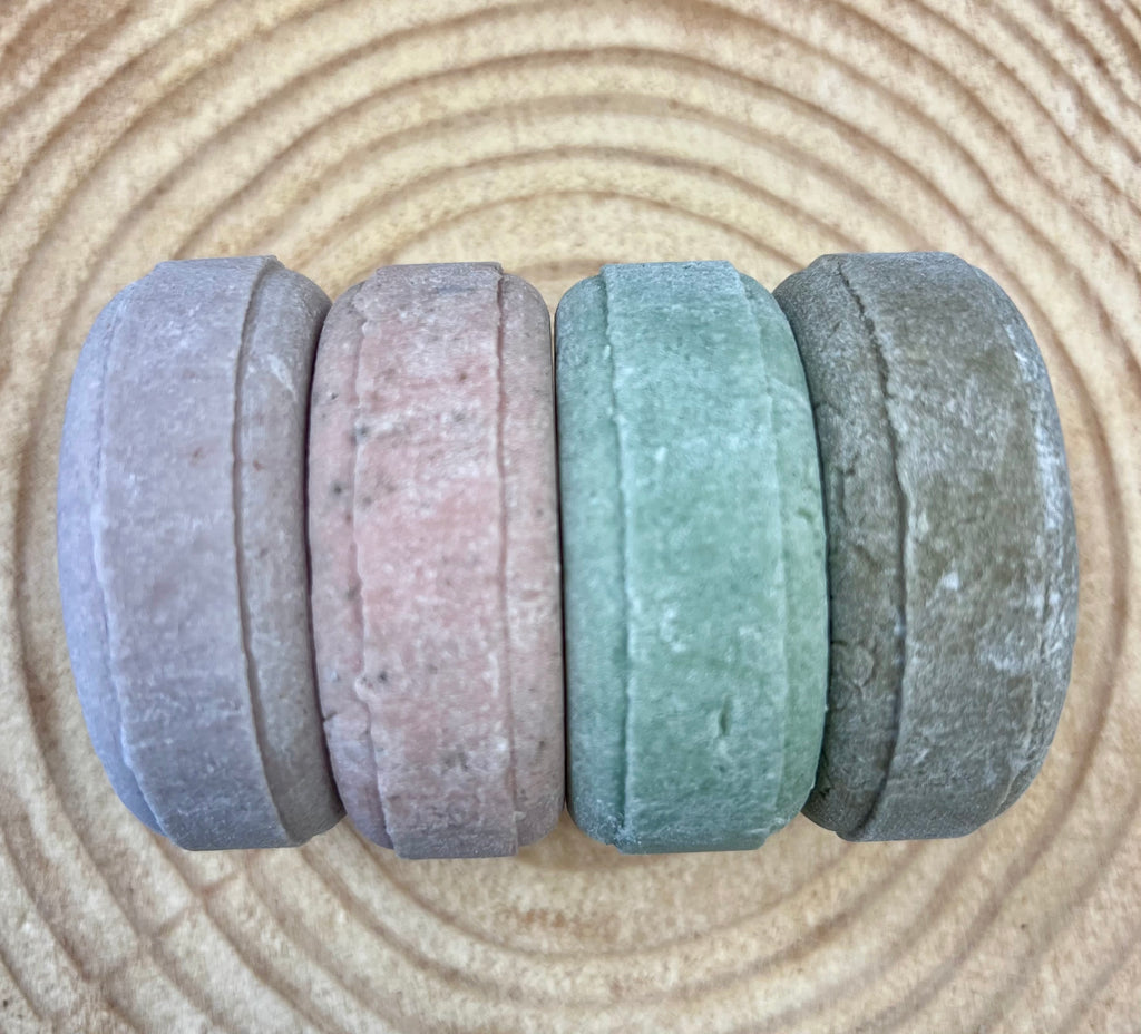 Four shampoo bars of different colors on a wood surface
