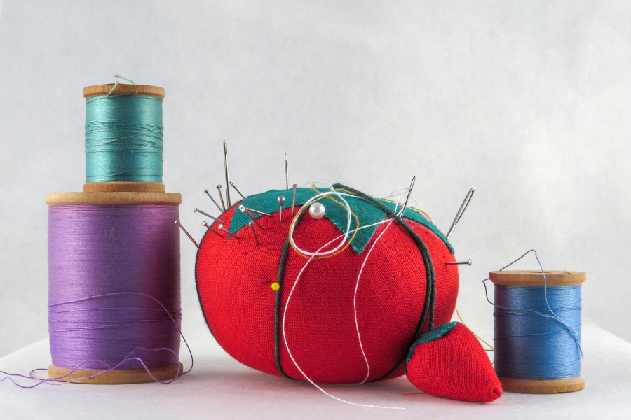 Red tomato-shaped pincushion with pins and spools of thread on a white background