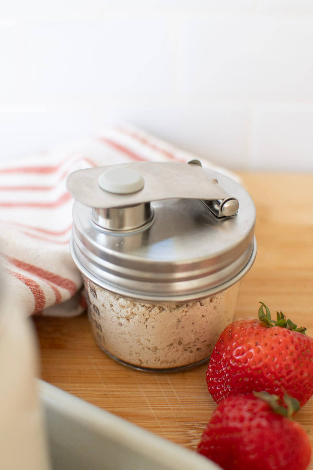 Stainless Steel pouring lid on a wide mouth jar with salt in it, on a white background on a wooden surface next to strawberries