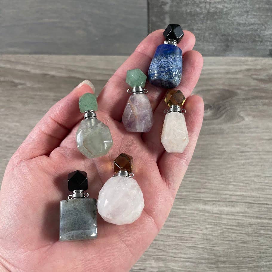 Hand holding various small stone containers with colored tops on a wooden surface