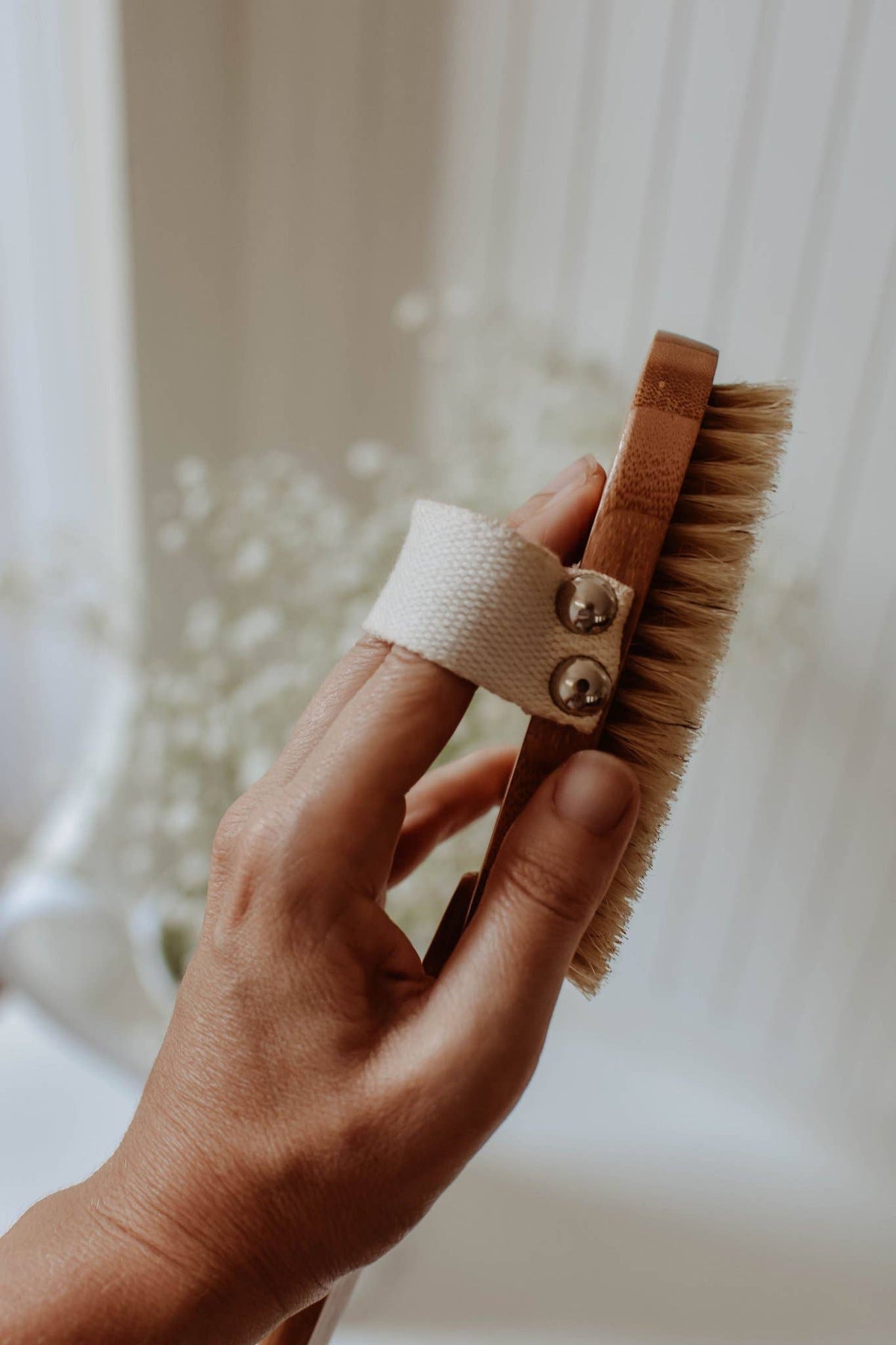 Hand holding a natural bristle brush with a white strap against a blurred background