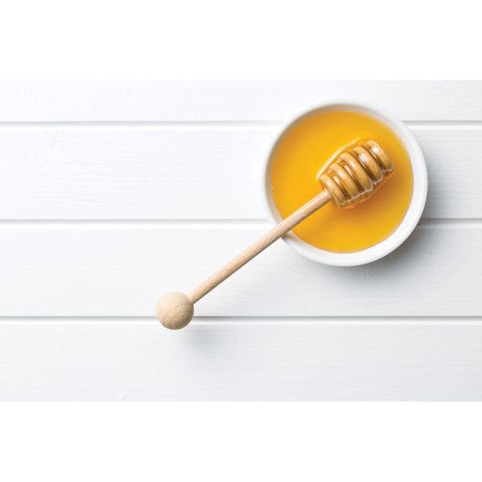 Mason jar with honey and a wooden dipper on a white background