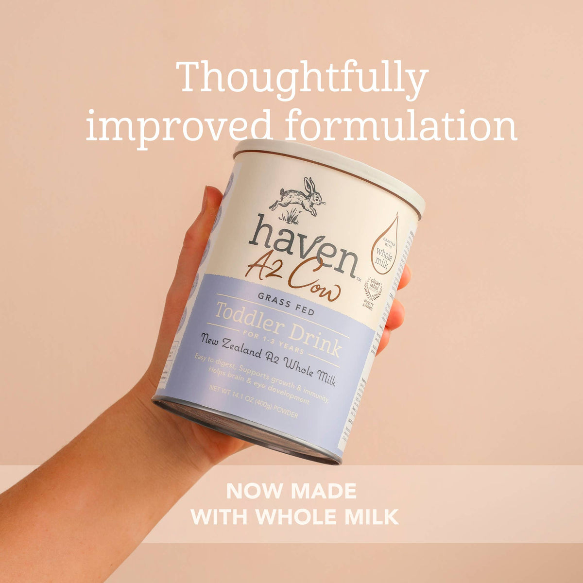 A hand holding a can of Haven A2 Cow Toddler Drink grass-fed whole milk formula against a soft peach background with promotional text overlays.