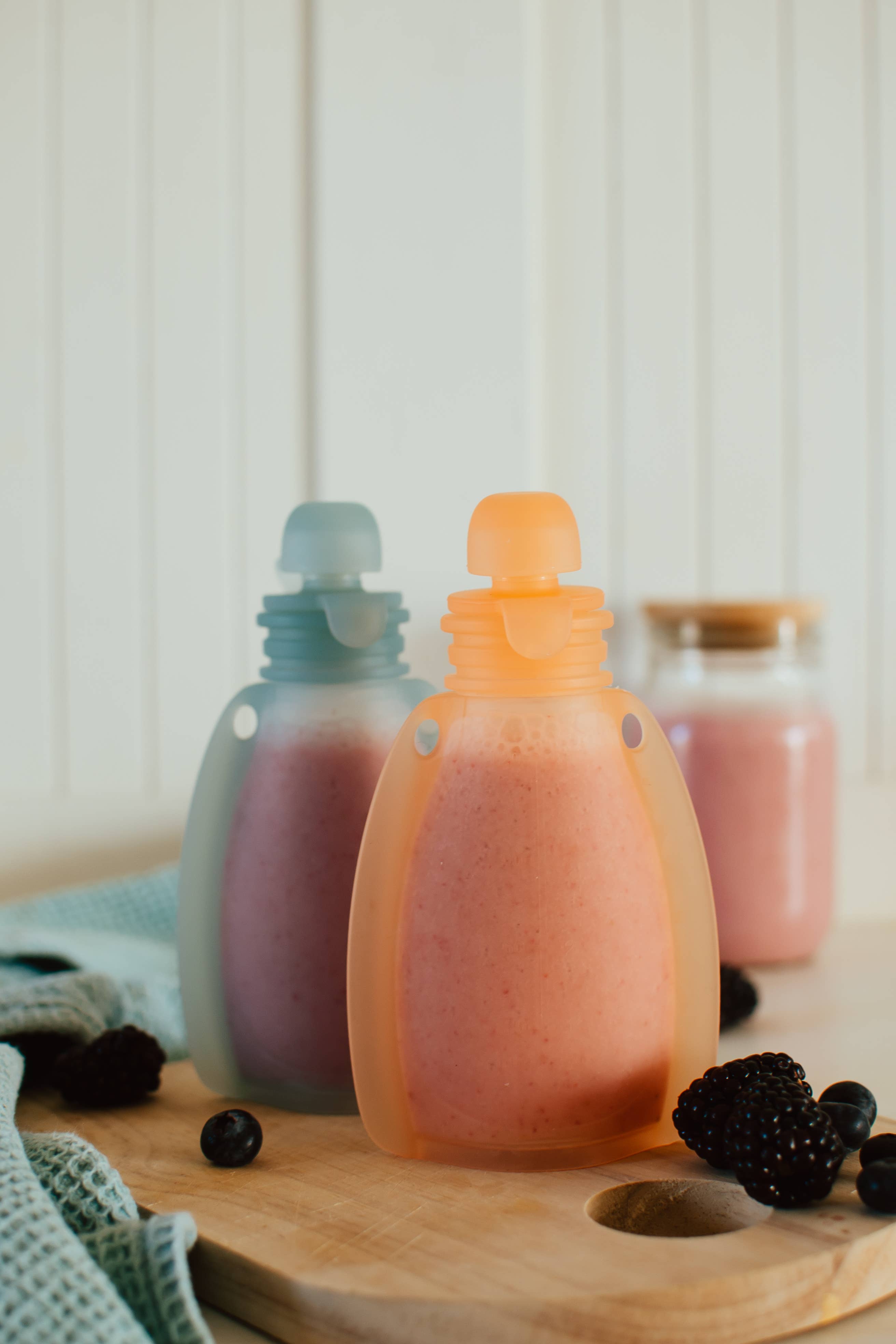 Two squeeze pouches filled with a pinkish liquid on a wooden surface with blackberries.