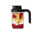 Glass jar with black lid and handle, filled with lemon and raspberry slices on a white background