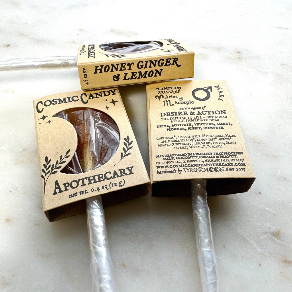 Two honey sticks in cardboard boxes labeled 'Honey Ginger & Lemon' and 'Cosmic Candy Apothecary' on a marble surface.