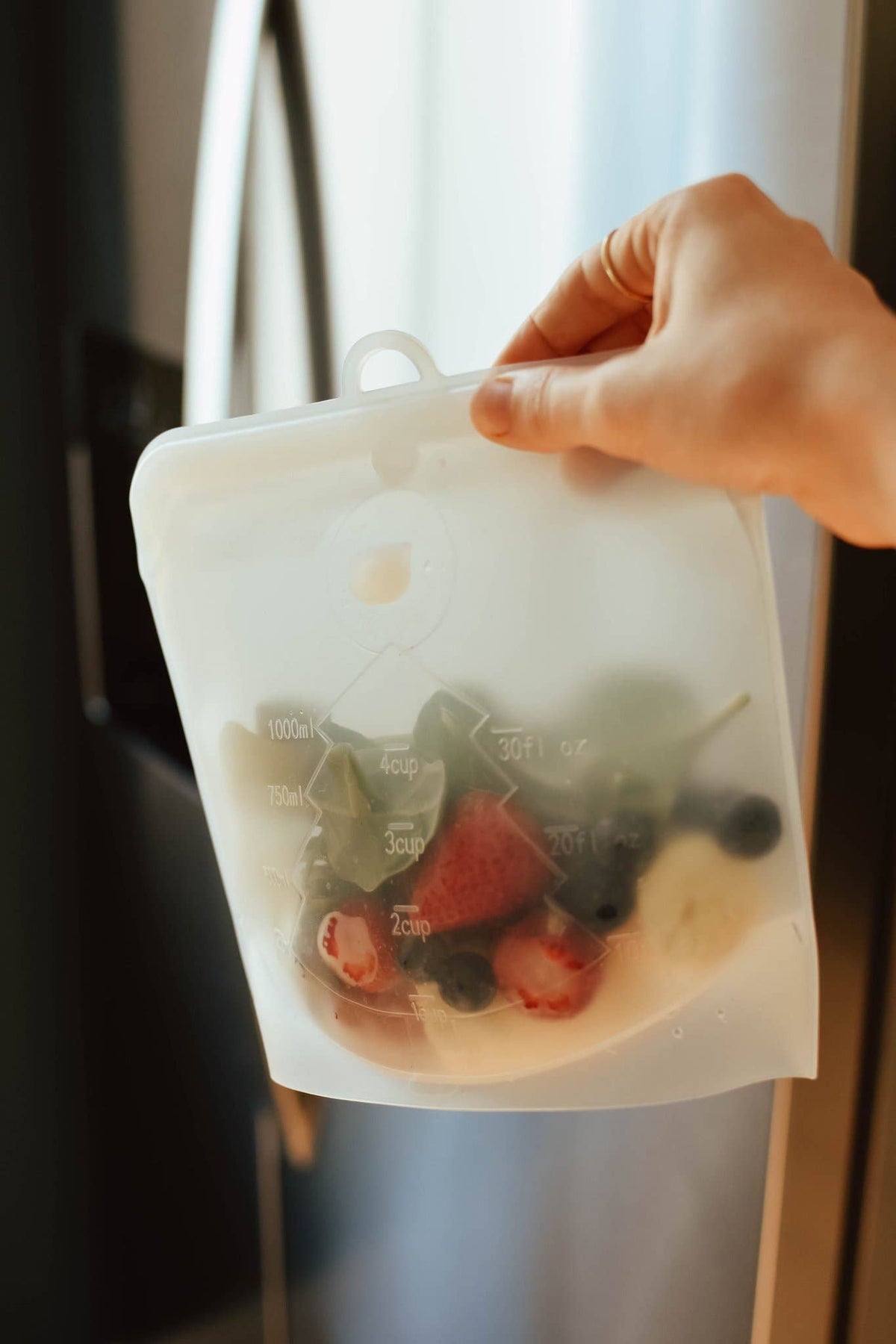 Hand holding a reusable silicone food storage bag with fruits and vegetables.