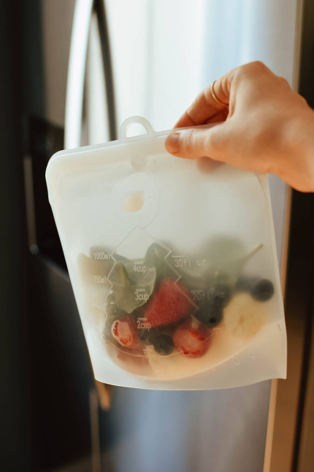 Hand holding a reusable silicone food storage bag with fruits and vegetables.