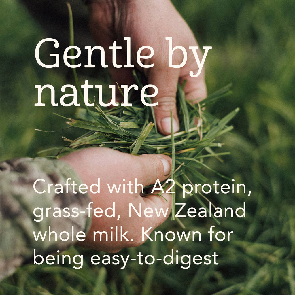 A close-up of two hands holding a handful of green grass in an outdoor field, with large white text reading 'Gentle by nature' and smaller text below stating 'Crafted with A2 protein, grass-fed, New Zealand whole milk. Known for being easy-to-digest.