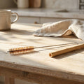 Bamboo straw and cleaning brush on a wooden surface with a cup and cloth in the background.