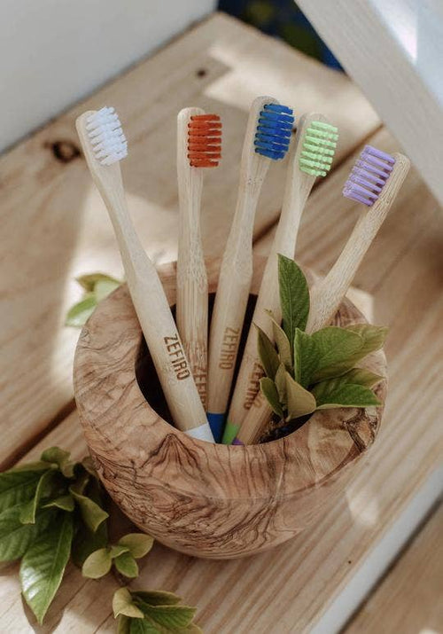 Set of five wooden toothbrushes with colored bristles in a wooden holder on a wooden surface.