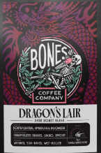 Bones Coffee Company Dragon's Lair coffee package with coffee beans and a cup on a dark surface