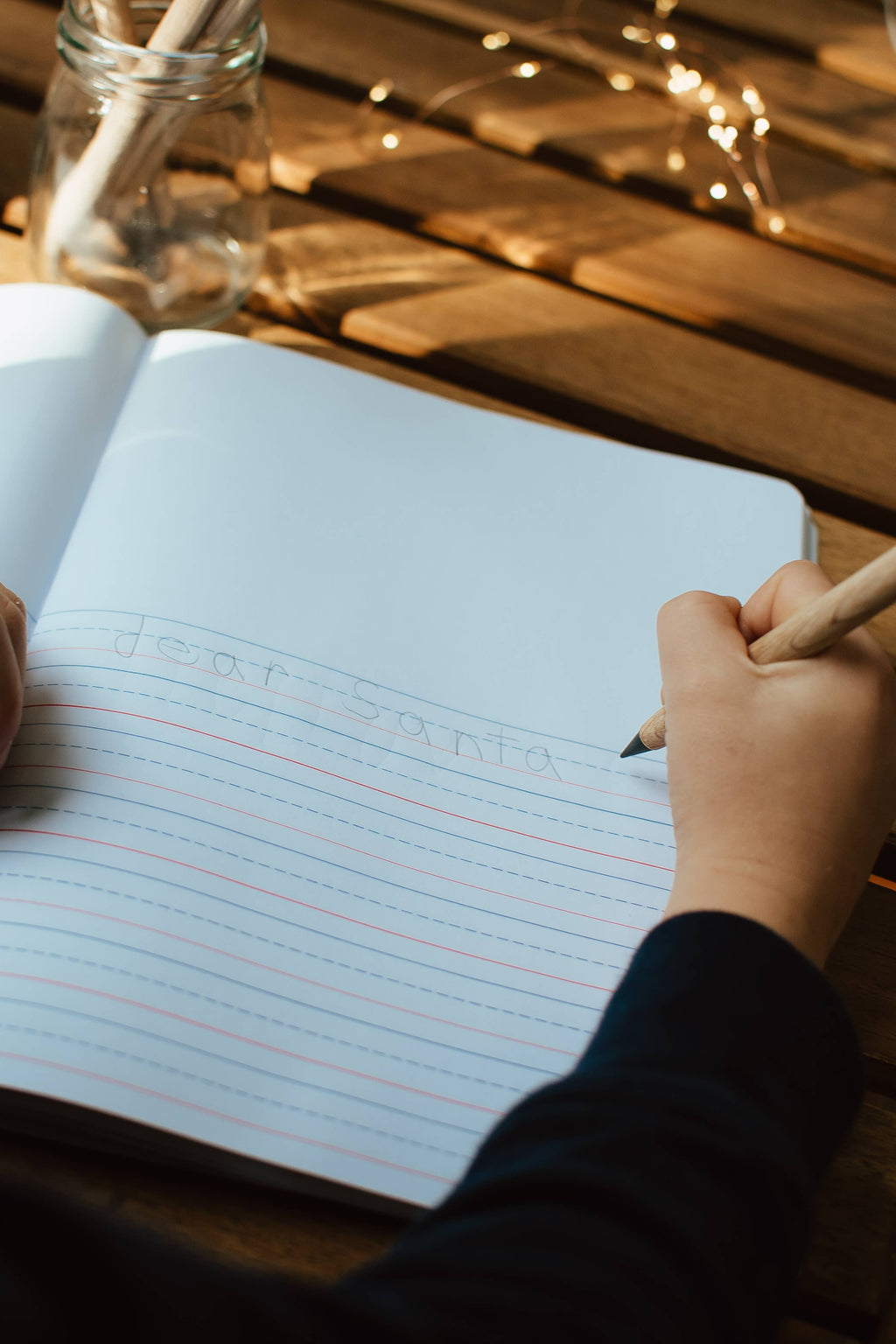 Hand writing in a notebook with a pencil on a wooden surface