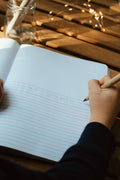 Hand writing in a notebook with a pencil on a wooden surface