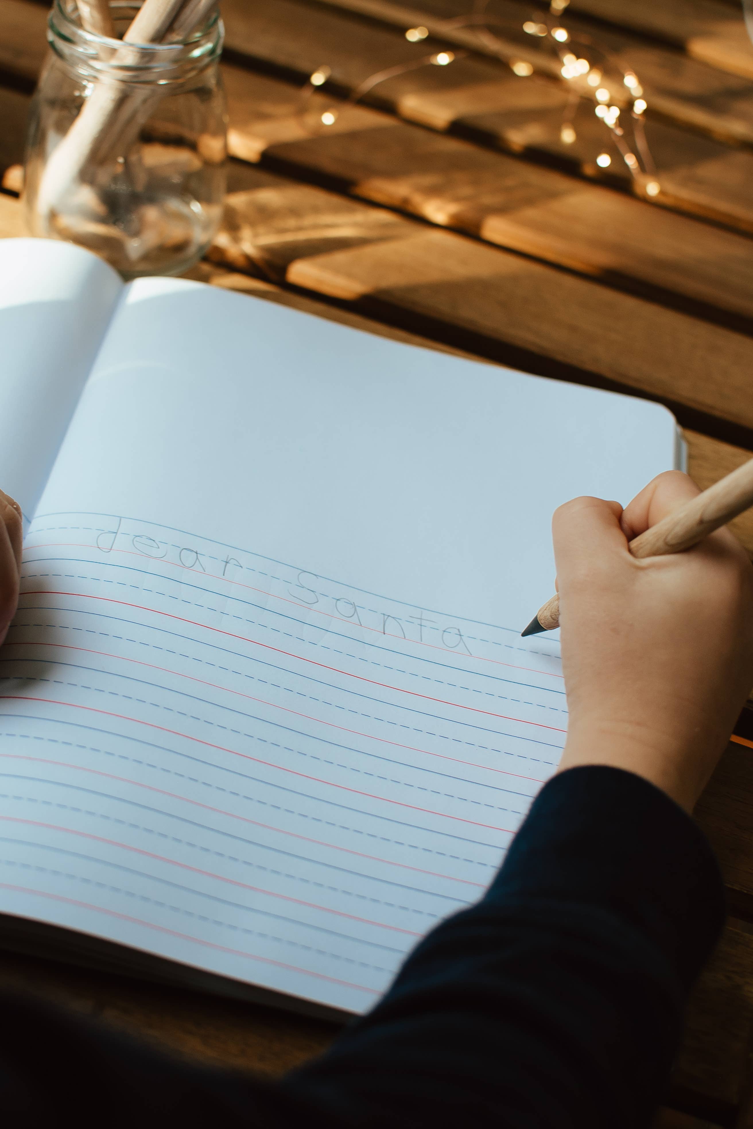 Hand writing in a notebook with a pencil on a wooden surface