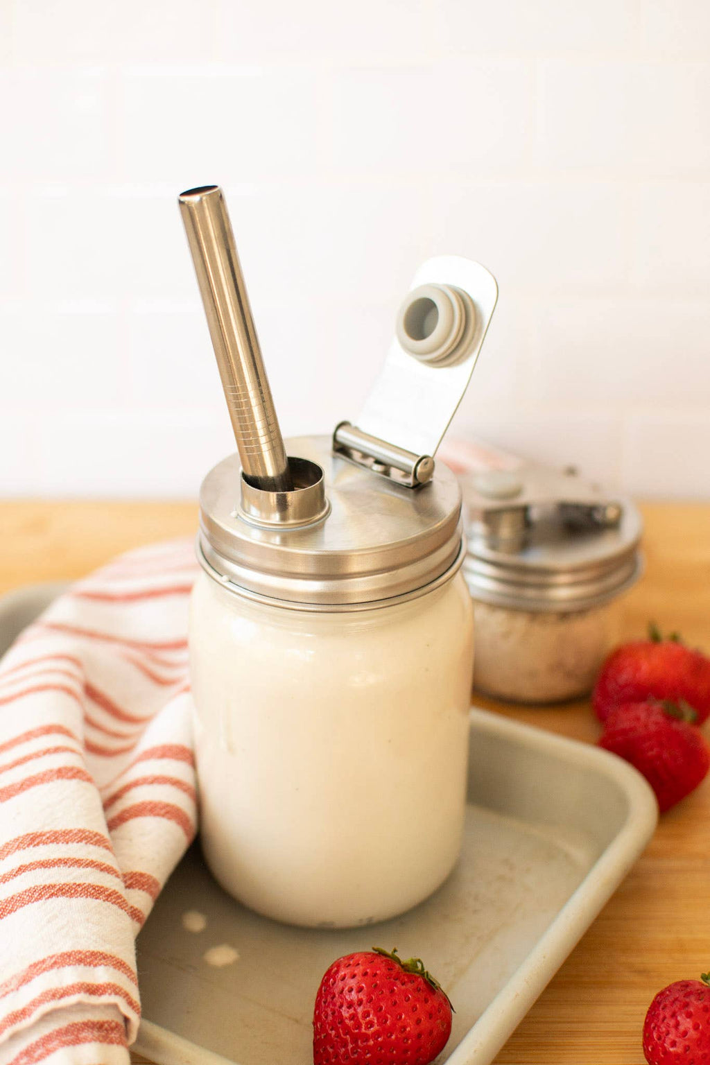 Glass jar with metal lid and straw on a tray with strawberries