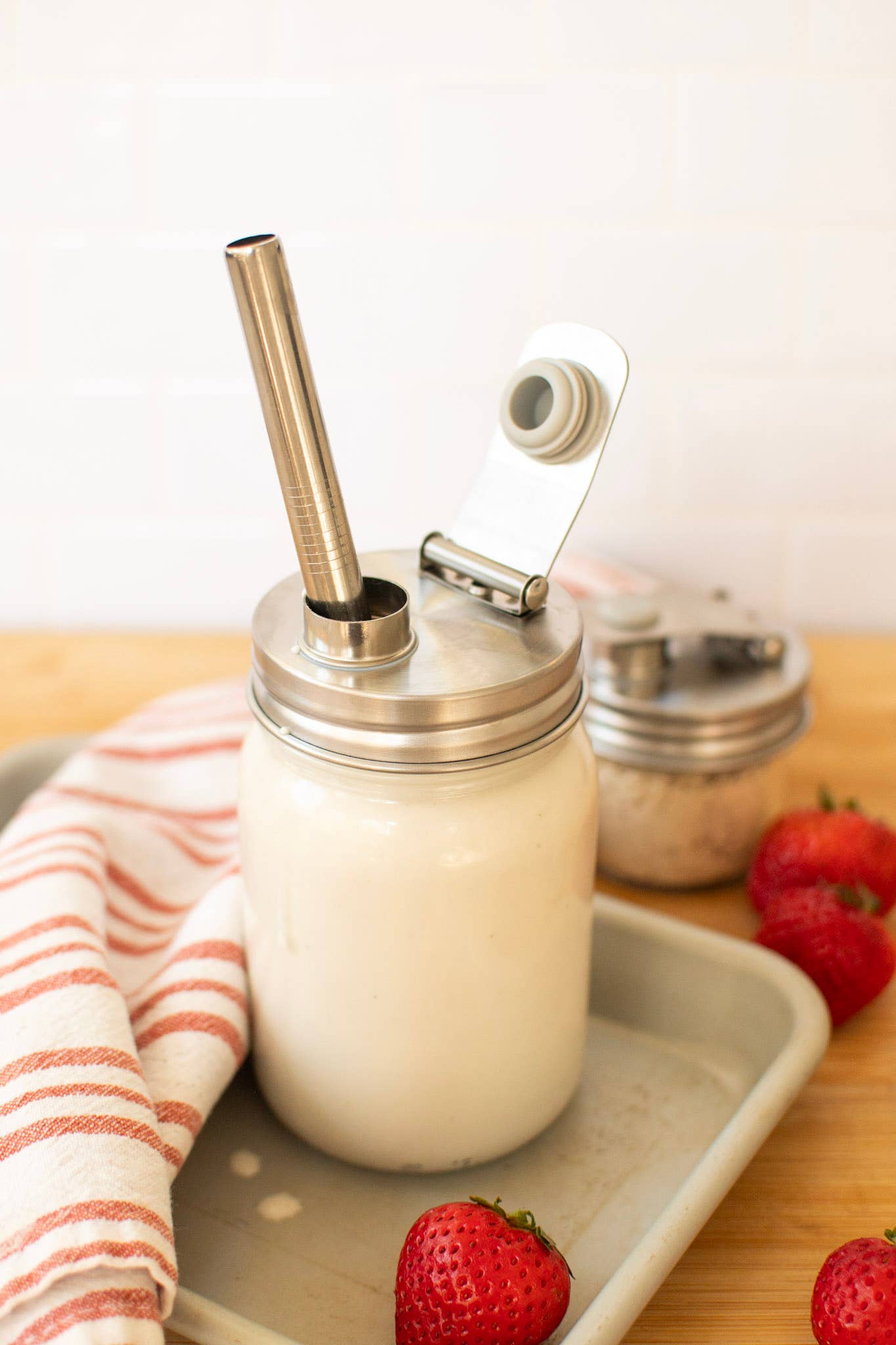 Glass jar with metal lid and straw on a tray with strawberries