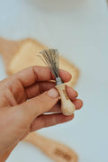 Hand holding a small whisk tool with wooden handle and metal head on a blurred background