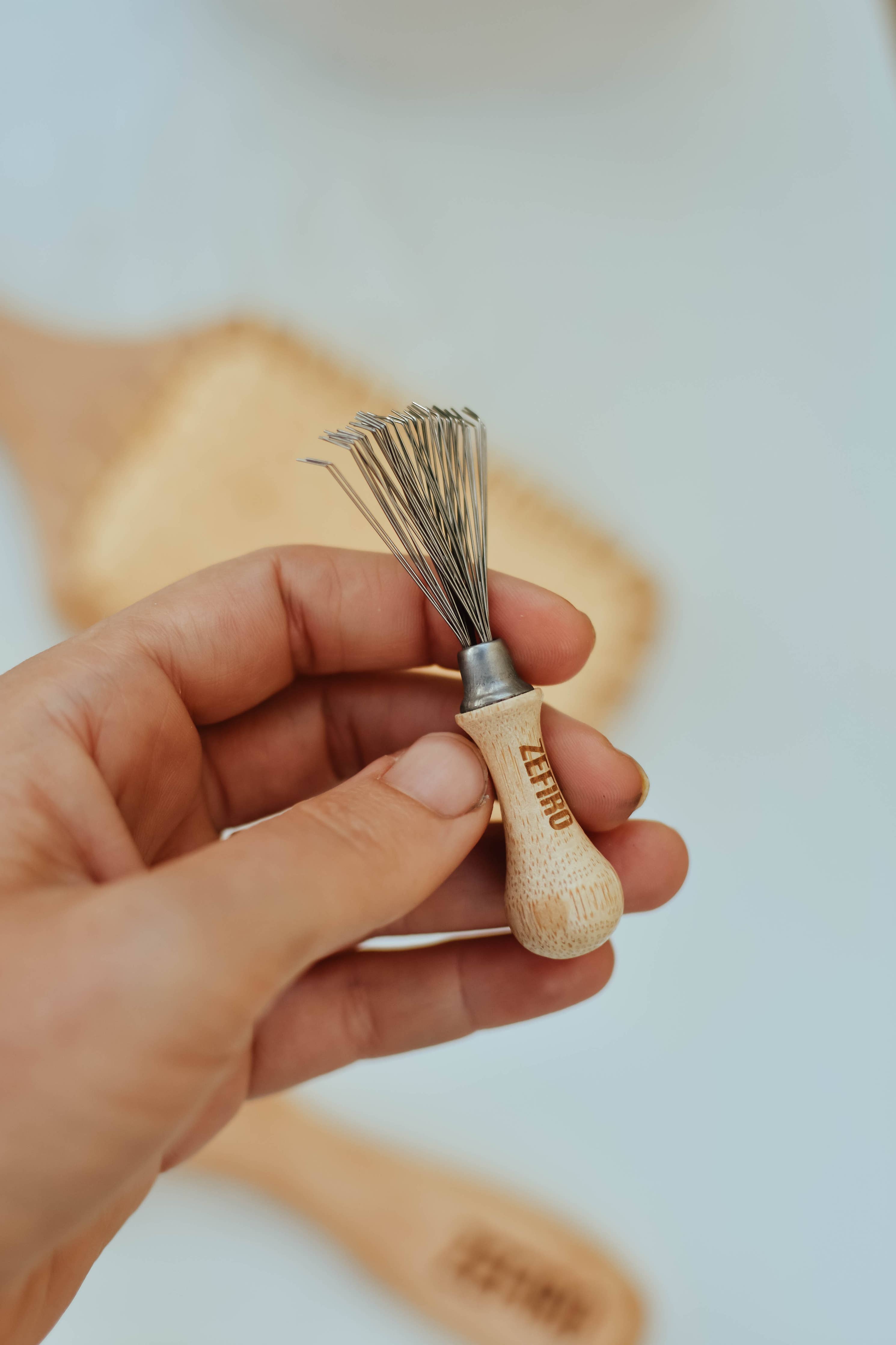 Hand holding a small whisk tool with wooden handle and metal head on a blurred background