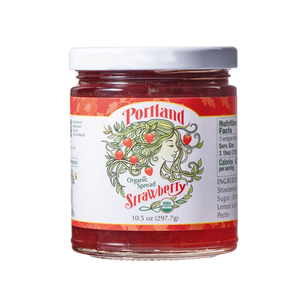 A glass jar of Portland Organic Spread Strawberry jam with a white lid and a white label featuring red strawberry graphics and the Portland brand name.